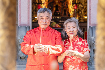 Obraz premium Celebrating Lunar New Year 2026 with cultural pride and warm greetings at a temple by a asian senior couple dressed in bright red traditional outfits expresses heartfelt wishes
