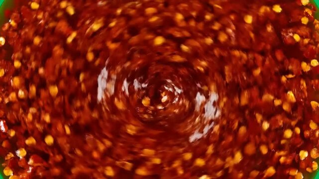 A close-up, top-down view of swirling, glistening chili flakes in a dark, rich sauce, creating a mesmerizing, textured pattern of red and orange hues