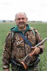 A hunter with a gun in camouflage clothing. A senior man with a gun, medium shot, searching for game.
