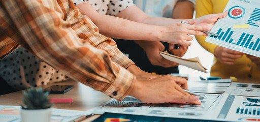 A diverse team engages in a collaborative business meeting, analyzing data charts and graphs on a table cluttered with digital devices, fostering teamwork and strategy. SACTR