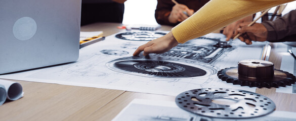 Engineers collaborate over detailed technical drawings and blueprints in a modern workspace, utilizing tools for innovative project planning and design analysis. SACTR