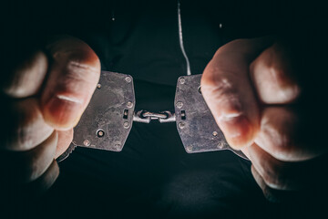 Hands gripping metal handcuffs tightly, showcasing the tension and struggle, with a dark background emphasizing the seriousness of the situation and the concept of restraint