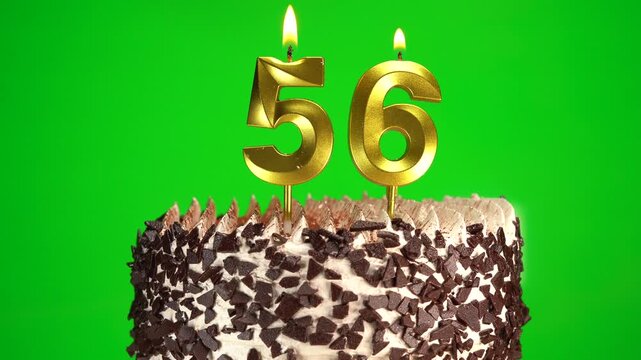 Lighting number 56 golden birthday candle on festive cake. Green screen, chromakey. Birthday cake on 56th anniversary