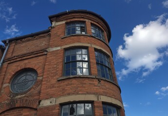 Fototapeta premium vintage brick building corner with arched windows and cloudy blue sky