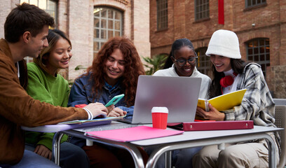 Cheerful group of multiracial student friends gathering together to study at university using a laptop computer outside school building. Image with copy space.