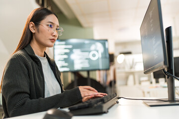 Focused female programmer coding on a computer in office. Young Asian software developer thinking and solving a problem. Women in tech concept