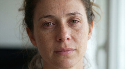 Fototapeta premium Woman with neutral expression gazing thoughtfully indoors near window, tear-stained eyes 