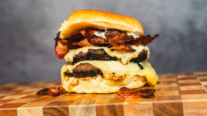 Delicious double deck bacon cheeseburger on a beautiful wooden board. Juicy patties, crispy bacon,...