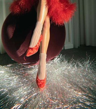 Female legs wearing red heels in fashion editorial setting. Surreal studio scene with glossy sphere and reflective foil.