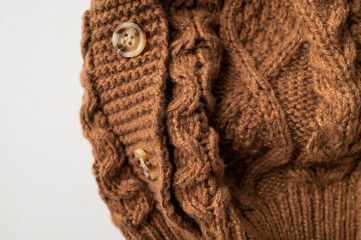 Close-up of brown knitted wool cotton sweater. Details of cozy winter or fall children's sweater, buttoned cardigan, pullover. Neckline detail, sleeves, large knit pattern. Trendy Color 2025