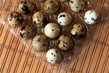 Fototapeta premium Quail eggs in a transparent plastic tray placed on a wooden surface. Concept of healthy lifestyle, proper nutrition, organic food products and natural protein source.