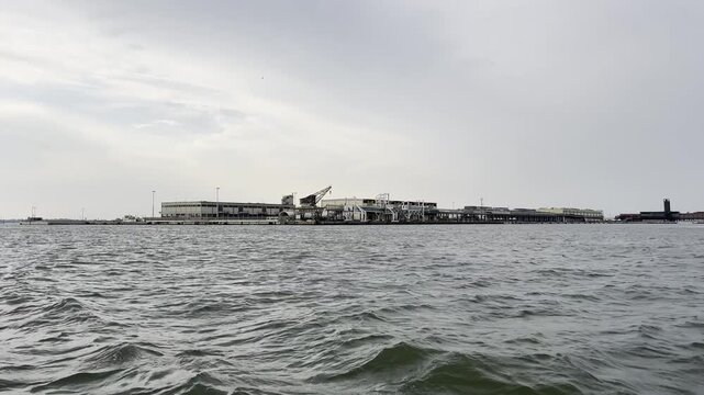 Industrial harbor skyline with moving water waves under cloudy sky captured over three frames