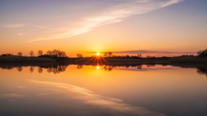 Naklejka premium Sun bursts over still water reflecting the sunset sky, with silhouetted trees
