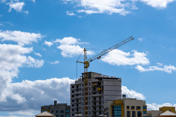 Fototapeta premium Tower Crane and Apartment Building Under Construction Against Cloudy Sky