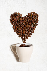 Coffee concept. Cup with scattered coffee beans in the shape of a heart on a white background, top view, closeup