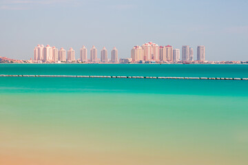 The Pearl Island in Doha, sunny coastal skyline with turquoise water and modern high-rise beachfront buildings across the horizon