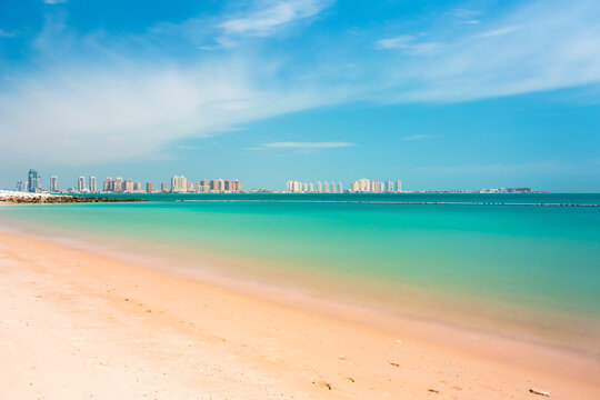 Panoramic view of The Pearl Island in Doha bright sunny beach with turquoise sea and distant city skyline under clear blue sky
