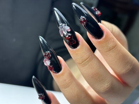 Glossy black stiletto nails featuring intricate 3D floral designs and deep red gemstones for a luxurious, gothic-inspired aesthetic.