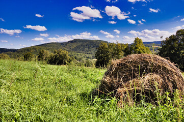 Malowniczy górski krajobraz z dużym snopem siana na zielonym polu pod błękitnym niebem. Góry Kaczawskie – widok na szczyt Dłużek. © Pol Badger