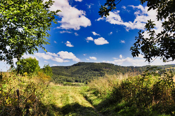 Szlak Słonecznej Łąki przez zalesione góry pod błękitnym niebem. Góry Kaczawskie – widok na szczyt Dłużek. © Pol Badger