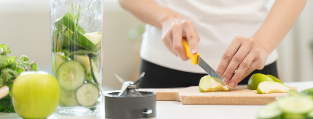 Woman putting fruit and vegetable into blender to make detox healthy drink.