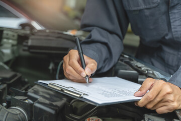 Auto check up and car service shop concept. Mechanic writing job checklist to clipboard to estimate...