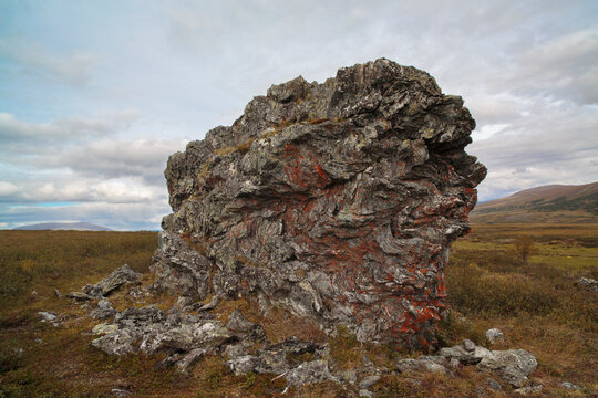 A large rock lies in a field. The rock is covered in moss and has a reddish tint. Polar Ural Mountains