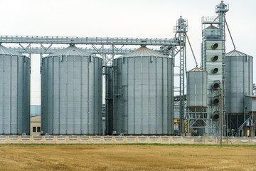 A large modern plant located near a wheat field for the storage and processing of grain crops. view of the granary illuminated by the light of the setting sun against the blue sky. harvest season.