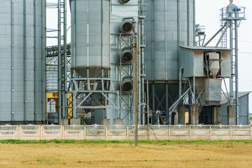 A large modern plant located near a wheat field for the storage and processing of grain crops. view of the granary illuminated by the light of the setting sun against the blue sky. harvest season.