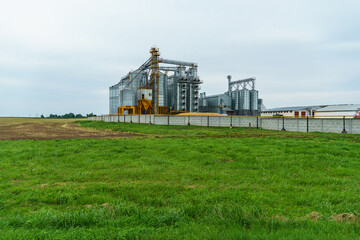 A large modern plant located near a wheat field for the storage and processing of grain crops. view of the granary illuminated by the light of the setting sun against the blue sky. harvest season.
