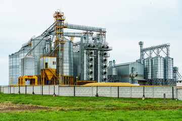 A large modern plant located near a wheat field for the storage and processing of grain crops. view of the granary illuminated by the light of the setting sun against the blue sky. harvest season.