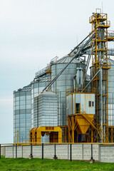 A large modern plant located near a wheat field for the storage and processing of grain crops. view of the granary illuminated by the light of the setting sun against the blue sky. harvest season.