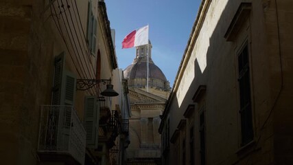 Malta national flag waving above historic church dome in narrow Mediterranean street