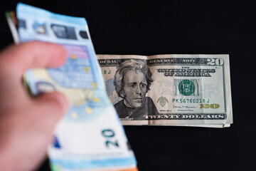 20 dollar banknotes on a black background and in the foreground 20 euro banknotes held in a hand