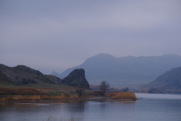 Autumn on the river Or in Kazakhstan, A calm landscape with mountains, river and autumn vegetation on a cloudy day.