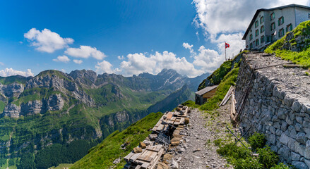 Naklejka premium Breathtaking Alpine Panorama at Schaefler Mountain Summit with Historic Chalet and Dramatic Peaks