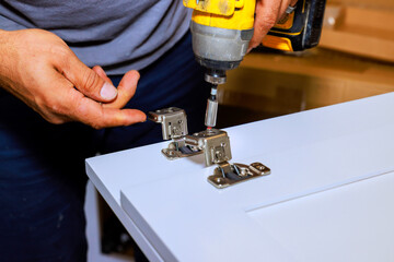 Carpenter uses power drill to attach hinges to cabinet in workshop setting.