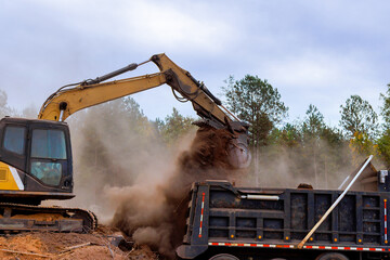 An excavator is actively transferring dirt into dump truck at construction site © ungvar