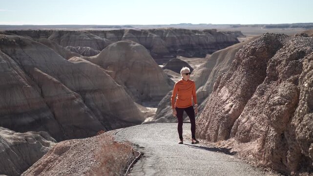 A mature woman walks along the path in Blue Mesa area of Petrified Forest National Park in Arizona. The landscape features eroded hills.