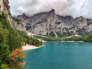 Turquoise Lago di Braies alpine lake surrounded by pine forest and dramatic rocky mountains partially covered by low clouds. Dolomites, South Tyrol, Italy