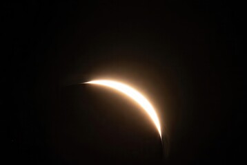 A radiant sliver of sun emerges during a partial solar eclipse, illuminating the vast dark sky