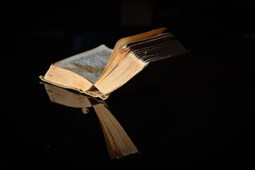 a small, very old book lying open on a dark, reflective surface. Book with pages yellowed with age, sense of historical depth. Dramatic, contemplative mood. For literary blogs, vintage themes.