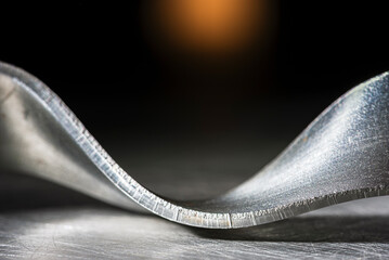 Bent steel flat bar like a ribbon, close-up of metal texture, cold, dark industrial atmosphere