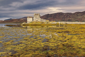 Sunny moment on a cloudy day lighting Eilean Donan tidal island-castle at low tide, linked to the mainland by a stone footbridge. Dornie-Scotland-186