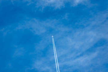 Obraz premium A passenger airplane flies high across a deep blue sky, leaving a long white contrail behind. Thin clouds emphasize the sense of height and motion.
