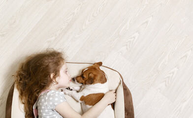Cute girl hugging and kissing a dog, lying on wood floor.