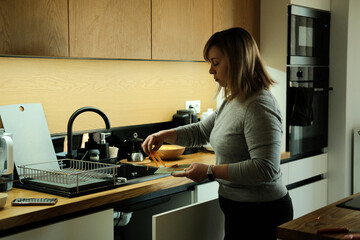 Woman stands in kitchen peeling carrot over sink. Zero waste lifestyle, organic waste, composting at home, sustainable living.