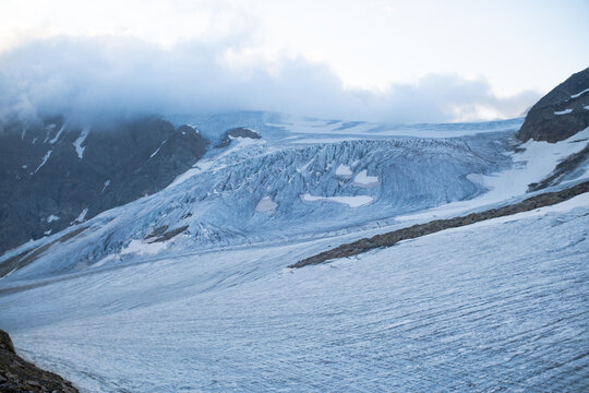 Large alpine glacier with crevasses and melting ice under clouds