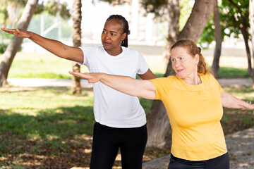 Diverse senior women performing tai chi exercises in a park, stretching their arms while focusing on balance and movement for physical wellness and health