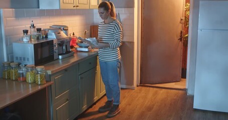 A young woman in casual clothes unrolls a roll of foil for baking in a bright, modern kitchen in the evening. Everyday routine, lifestyle.